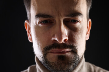 Obraz premium Sad man crying on black background, closeup