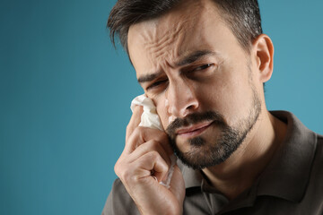 Sad man with paper tissue crying on light blue background, space for text