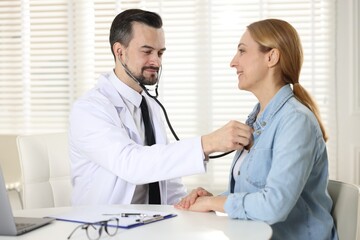 Fototapeta premium Cardiologist with stethoscope listening patient's heartbeat at desk in clinic