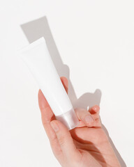 Hand holding blank white plastic tube on white background. Cosmetic beauty product branding mockup. Copy space