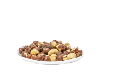 A white plate filled with roasted hazelnuts, some with peels and others peeled. Close-up side view macro photography, enlightened and isolated on a bright white transparent background with copy space