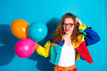 Young woman in vibrant fashion with balloons against bright blue background