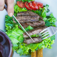 Woman cutting meat on plate with fork and knife in restaurant 