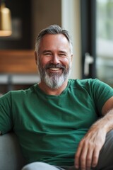 Obraz premium Bearded man in green shirt smiling and sitting on couch.