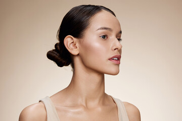 Beautiful woman with a natural makeup look against a warm beige background, showcasing healthy skin and minimalist fashion style