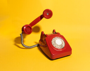 A striking red vintage rotary telephone sits on a bold yellow background. This nostalgic communication device blends retro aesthetics with a vibrant, minimalist composition, perfect for vintage-themed