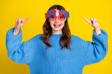 Cheerful young woman in stylish blue sweater and heart-shaped glasses posing against a vibrant...