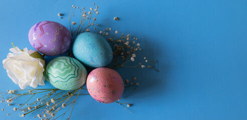 Top view of colored Easter eggs and flowers. Blue background with copy space