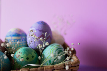 Hand painted Easter eggs in wicker basket. Pastel background