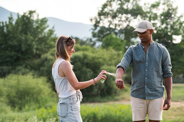 Young couple spraying tick repellent on her legs and arms during a summer nature trip
