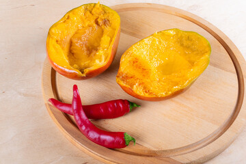 Two halves of mango and two red chili peppers on wooden cutting board