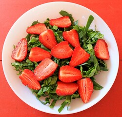 Strawberry salad with arugula and spinach on red background