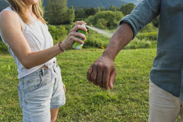 Young couple spraying tick repellent on her legs and arms during a summer nature trip