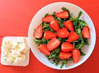 Strawberry salad with arugula and spinach on red background