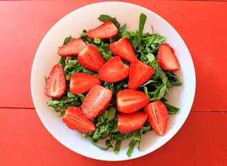 Strawberry salad with arugula and spinach on red background