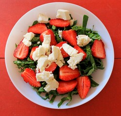 Strawberry salad with arugula and spinach on red background