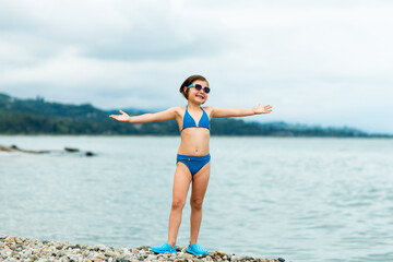 A small, beautiful girl in a blue swimsuit and sunglasses