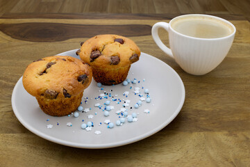 A plate of muffins and a cup of coffee sit on a table