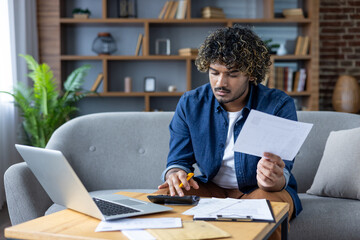 Man working at home with documents, bills and checks. Using laptop and calculator to calculate...