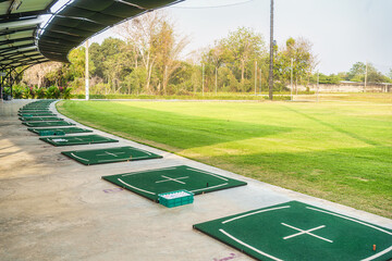 Fototapeta premium Golf driving range with multiple tee areas under shaded canopy, surrounded by lush green grass for leisure activity, sport practice