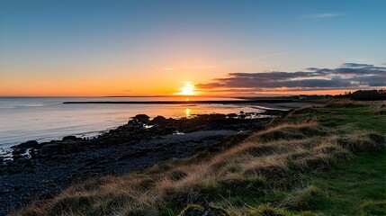Obraz premium Golden Sunset Over Calm Ocean With Rocky Beach And Grassy Shore
