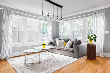 A cozy living room with a black chandelier above neutral furniture with yellow accents and an area rug on a hardwood floor.