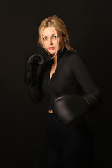 Girl isolated on black background in black clothes in boxing gloves. Woman doing sports. Boxing equipment. Woman and boxing.