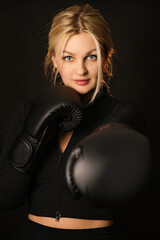 Girl isolated on black background in black clothes in boxing gloves. Woman doing sports. Boxing equipment. Woman and boxing.