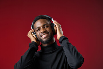 Young African man enjoying music with headphones, wearing a black turtleneck against a red background, conveying happiness and relaxation