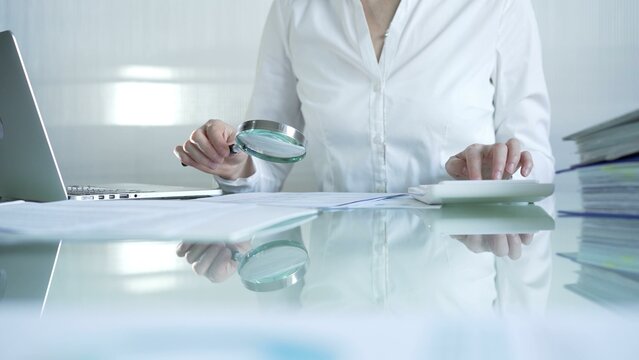 Businesswoman analyzing financial data with magnifying glass and calculator, performing accounting and auditing tasks in office. Audit and taxes theme in business