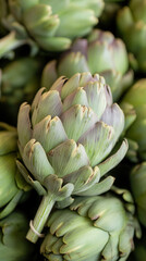 Obraz premium Vibrant display of fresh artichokes showcasing unique green and purple hues at a bustling market on a sunny day