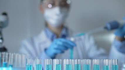 Laboratory tubes are in focus, closeup view. Female scientist researcher is using a micropipette at...