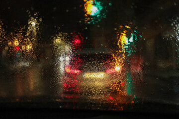 rainy-night atmosphere through the windshield of a car, with raindrops sharply in focus on the glass