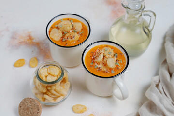 Roasted butternut squash soup with cream and pumpkin seeds on two white mugs.