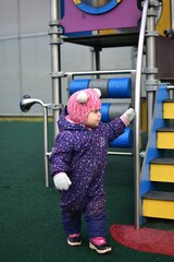 Baby girl playing in children playground in city park in cold weather autumn. Toddler girl having fun in public playground in winter