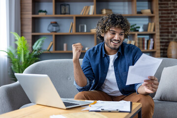 Successful satisfied man working with documents and bills at home, sitting on sofa in living room,...