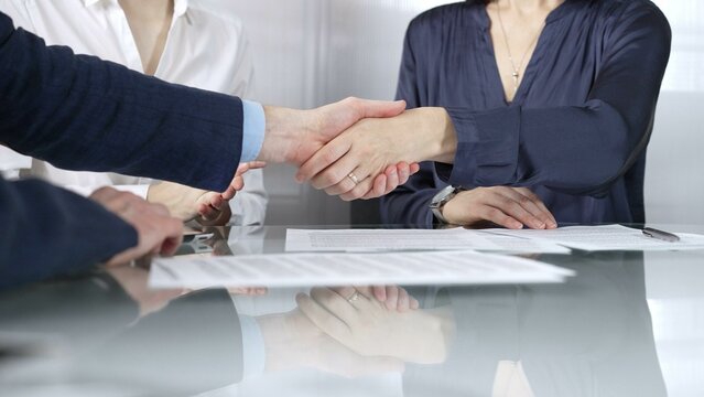 Unrecognizable business partners shaking hands after signing contract at glass table in office meeting, making a deal and closing agreement, close up of handshake