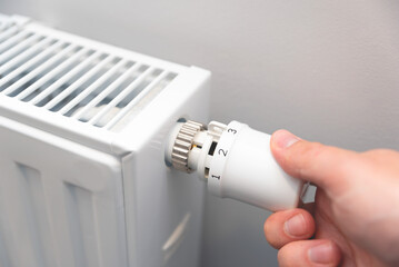 Modern white radiator, hand holding thermostat