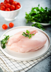Raw chicken breast for cooking is on a plate with herbs and vegetables