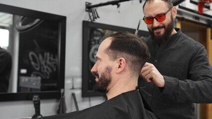 Fototapeta premium Skilled barber working on male client's hairstyle, carefully combing and preparing precision cut in contemporary barbershop setting
