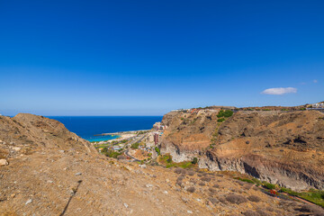 Coastal landscape with rocky hills overlooking Atlantic ocean and beach resort under clear sunny sky. Gran Canaria, Las Palmas, Spain.