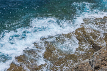 Waves of Atlantic Ocean crashing against rocky shore on Gran Canaria creating white foam and splashes. Spain.