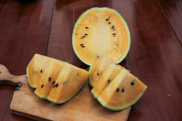 Close up of a yellow watermelon half and yellow watermelon triangle  shape slice with seeds on wooden cutting board, tropical fruits, dessert food