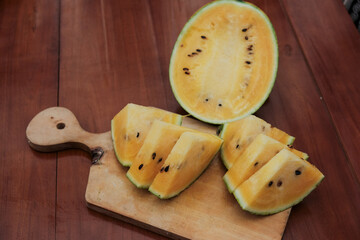 Close up of a yellow watermelon half and yellow watermelon triangle  shape slice with seeds on wooden cutting board, tropical fruits, dessert food