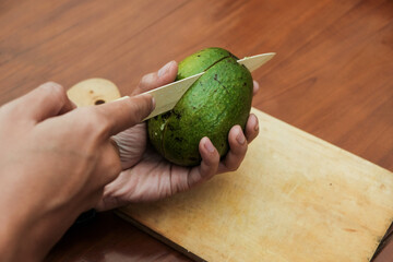 Close up of male hands cutting avocado with kitchen knife on wooden cutting board. Fresh ripe...