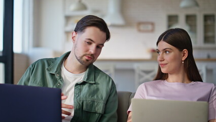 Closeup colleagues working laptops at living room interior. Talking pair work