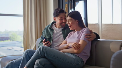 Obraz premium Man woman looking smartphone rejoicing success home sofa. Pair winning lottery
