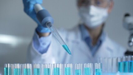 Woman scientist researcher using a micropipette to fill up test tubes with a blue liquid in...