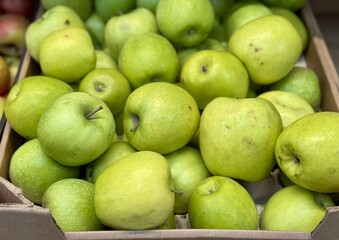 Box filled with fresh natural bio organic green apples placed on counter in local food market....