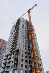 High-rise building under construction with a yellow crane next to it. Several floors with concrete balconies and windows visible. Some windows are covered with black plastic
